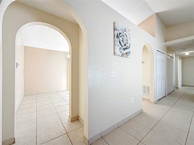 hallway featuring lofted ceiling, light tile patterned flooring, and a textured ceiling