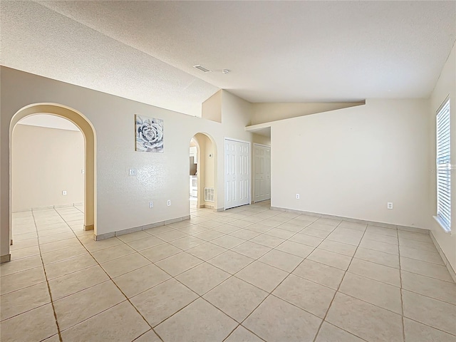 tiled spare room featuring lofted ceiling and a textured ceiling