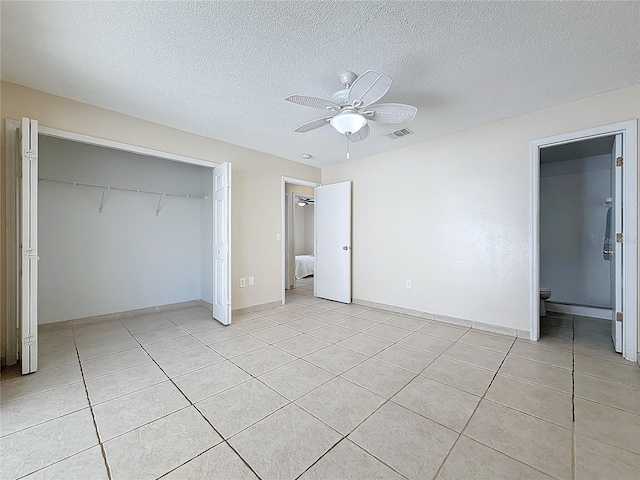 unfurnished bedroom with ceiling fan, ensuite bathroom, a textured ceiling, a closet, and light tile patterned floors