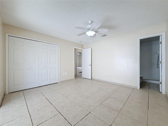 unfurnished bedroom featuring ceiling fan, light tile patterned floors, a textured ceiling, connected bathroom, and a closet