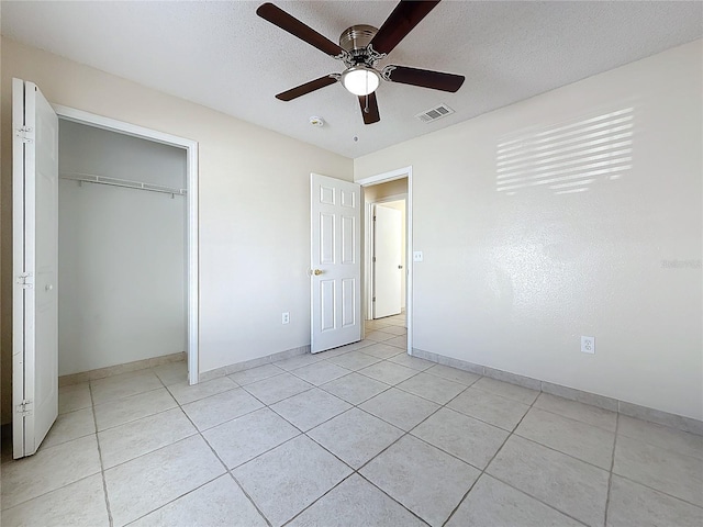 unfurnished bedroom with ceiling fan, a closet, light tile patterned flooring, and a textured ceiling