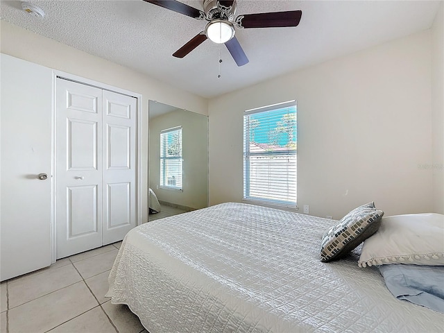 bedroom with ceiling fan, a closet, light tile patterned floors, and a textured ceiling