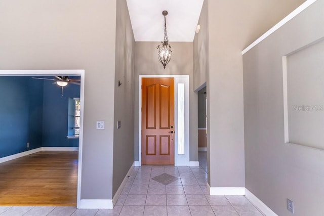 entryway with a towering ceiling, ceiling fan with notable chandelier, and light tile patterned flooring