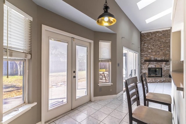 entryway featuring french doors, a healthy amount of sunlight, a brick fireplace, lofted ceiling with skylight, and light tile patterned floors