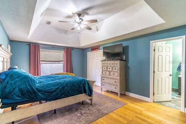 bedroom with ceiling fan, a closet, a raised ceiling, and light hardwood / wood-style flooring