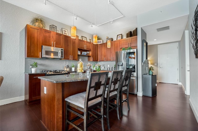 kitchen featuring appliances with stainless steel finishes, rail lighting, a breakfast bar, a kitchen island with sink, and decorative light fixtures