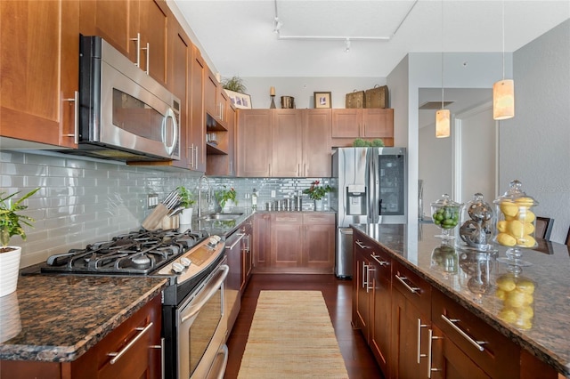 kitchen with sink, hanging light fixtures, dark stone counters, track lighting, and appliances with stainless steel finishes