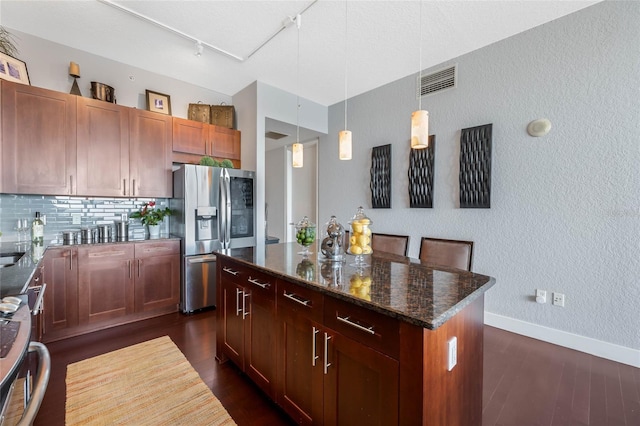 kitchen with stainless steel refrigerator with ice dispenser, dark stone countertops, pendant lighting, a kitchen island, and range