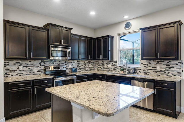 kitchen with stainless steel appliances, sink, light stone counters, decorative backsplash, and a kitchen island