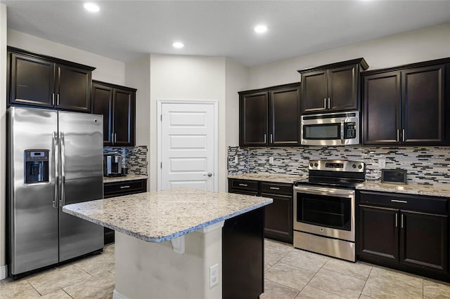 kitchen with light stone counters, a center island, stainless steel appliances, light tile patterned floors, and decorative backsplash