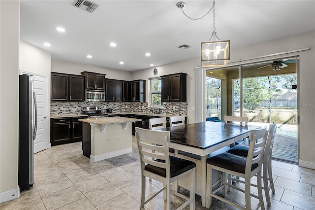 kitchen featuring appliances with stainless steel finishes, a center island, light tile patterned floors, pendant lighting, and tasteful backsplash