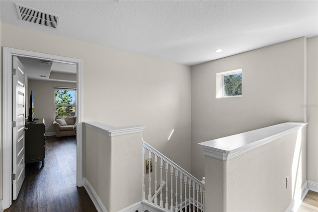 hall with a textured ceiling, a healthy amount of sunlight, and dark hardwood / wood-style floors