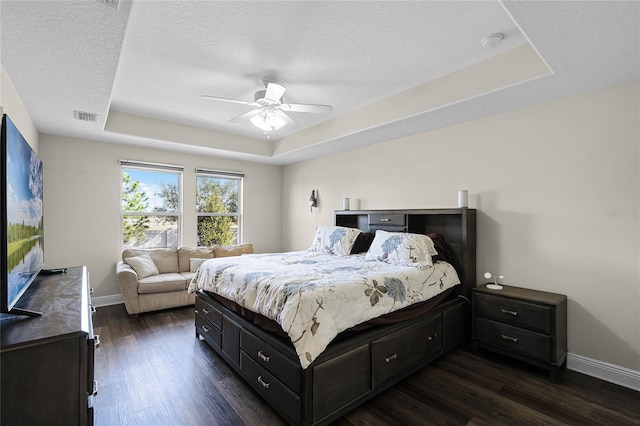 bedroom featuring a raised ceiling, a textured ceiling, ceiling fan, and dark wood-type flooring