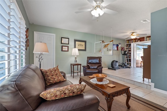 living area featuring light tile patterned floors, visible vents, baseboards, ceiling fan, and a textured ceiling