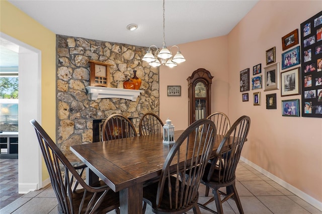 tiled dining space with a chandelier, a fireplace, and baseboards