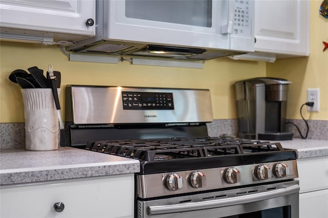 kitchen with stainless steel gas range, white cabinetry, white microwave, and light countertops