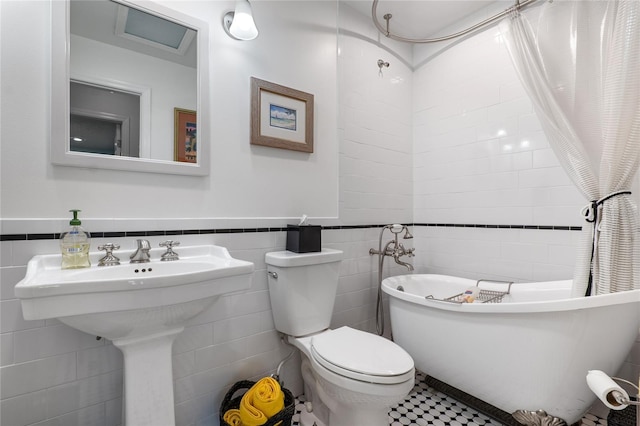 bathroom featuring a freestanding tub, wainscoting, tile walls, and toilet