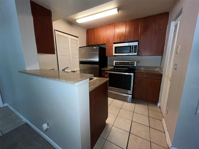 kitchen featuring light tile patterned floors, kitchen peninsula, light stone counters, and appliances with stainless steel finishes