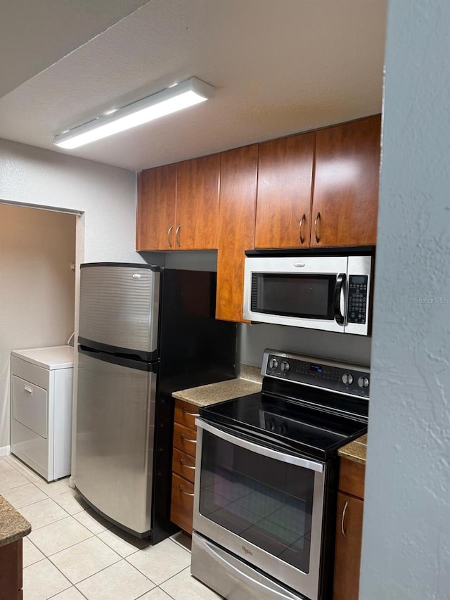 11538 Westwood Blvd Unit 226, Orlando, FL 32821 - kitchen with stainless steel appliances, washer / dryer, light tile patterned floors, and brown cabinetry