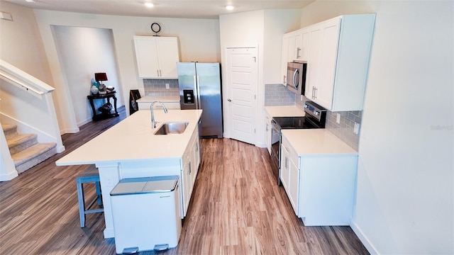 kitchen featuring white cabinetry, sink, backsplash, stainless steel appliances, and a center island with sink