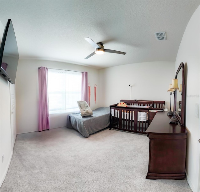 bedroom with ceiling fan, light carpet, and a textured ceiling