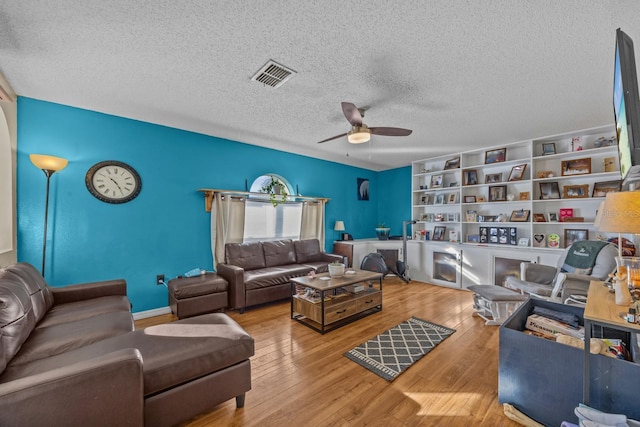 living room with a textured ceiling, light wood-type flooring, built in features, and ceiling fan