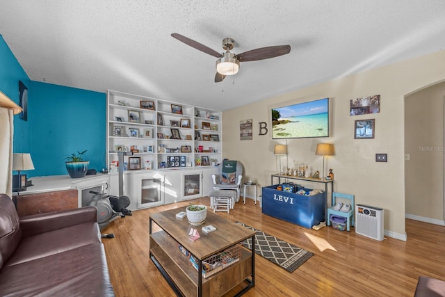 living room with ceiling fan, built in features, a textured ceiling, and light wood-type flooring