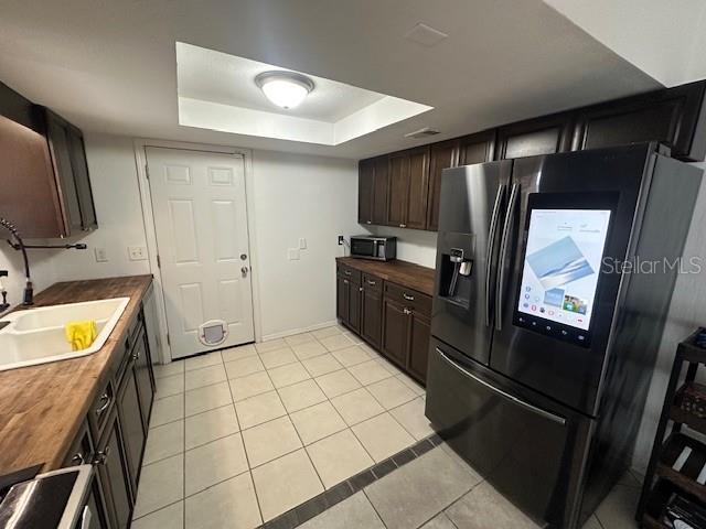 kitchen featuring sink, a raised ceiling, refrigerator with ice dispenser, butcher block countertops, and light tile patterned floors