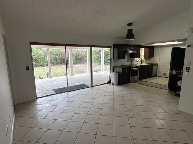 kitchen with electric stove, sink, vaulted ceiling, light tile patterned floors, and a textured ceiling