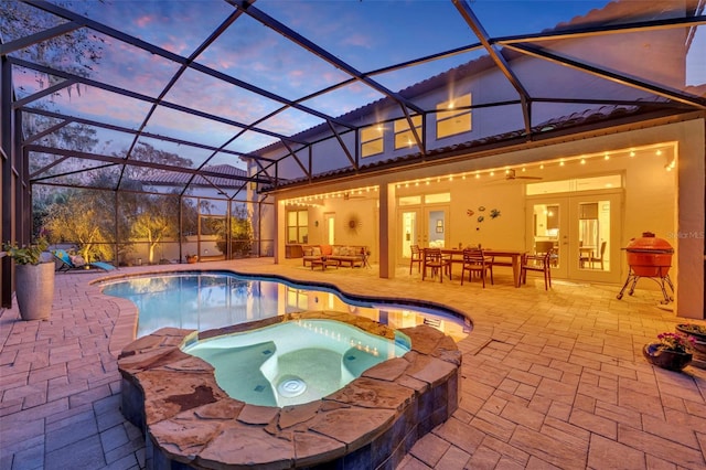 pool at dusk with outdoor lounge area, glass enclosure, a patio area, french doors, and an in ground hot tub