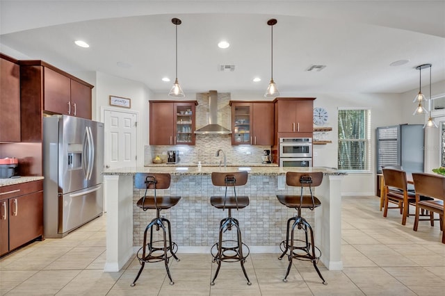 kitchen featuring wall chimney range hood, a kitchen breakfast bar, hanging light fixtures, and appliances with stainless steel finishes