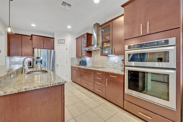 kitchen with appliances with stainless steel finishes, tasteful backsplash, sink, hanging light fixtures, and wall chimney exhaust hood