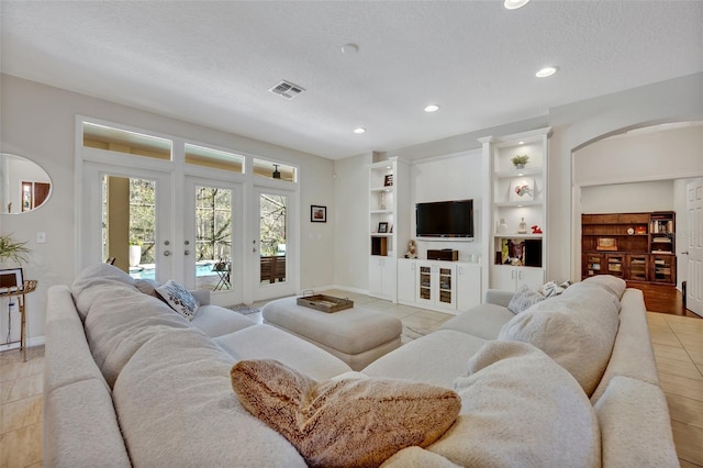 tiled living room featuring french doors, built in features, and a textured ceiling