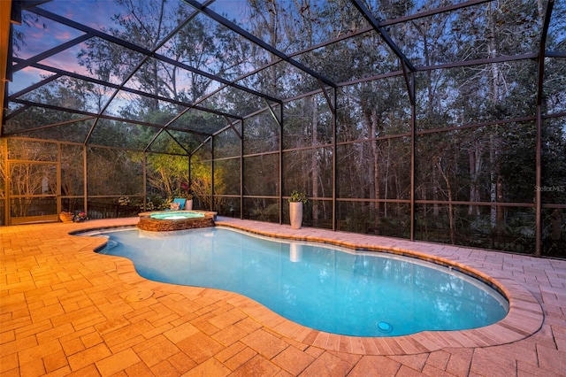 pool at dusk featuring an in ground hot tub, glass enclosure, and a patio