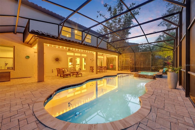 pool at dusk with an in ground hot tub, an outdoor hangout area, glass enclosure, and a patio