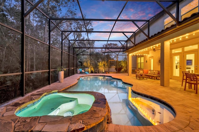 pool at dusk with ceiling fan, a patio, glass enclosure, an outdoor living space, and an in ground hot tub