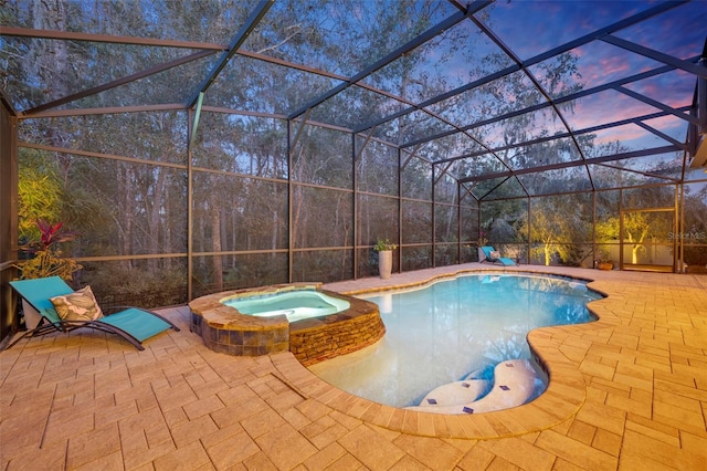 pool at dusk with an in ground hot tub, a lanai, and a patio area