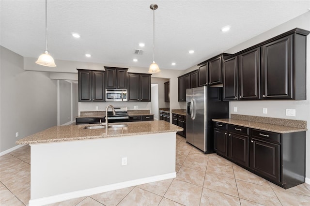 kitchen with stainless steel appliances, a kitchen island with sink, sink, pendant lighting, and light tile patterned flooring