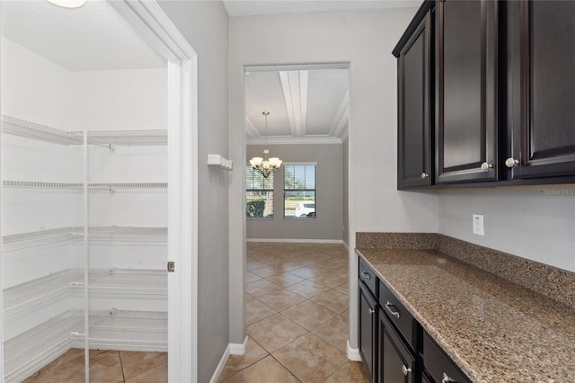 kitchen with light tile patterned floors, dark stone counters, an inviting chandelier, and ornamental molding