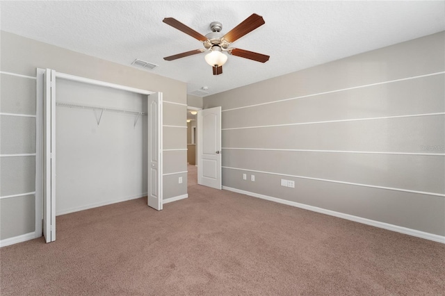 unfurnished bedroom with a textured ceiling, a closet, light colored carpet, and ceiling fan