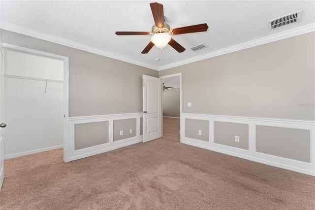 unfurnished bedroom featuring ceiling fan, light colored carpet, a textured ceiling, a closet, and ornamental molding