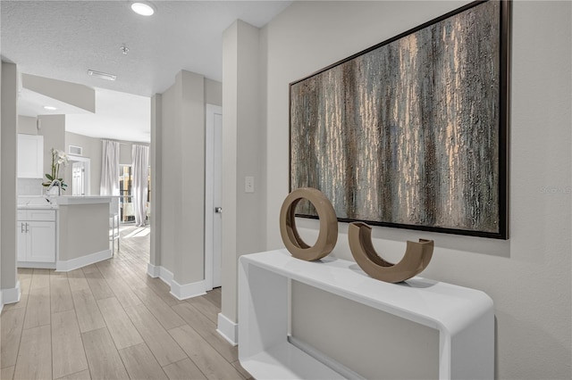 hallway with a textured ceiling and light hardwood / wood-style flooring