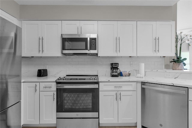 kitchen featuring white cabinets, appliances with stainless steel finishes, tasteful backsplash, and light stone counters