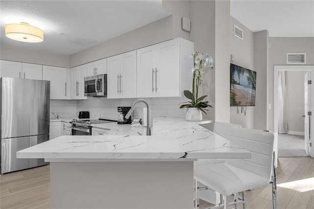 kitchen with kitchen peninsula, appliances with stainless steel finishes, white cabinetry, and light stone counters