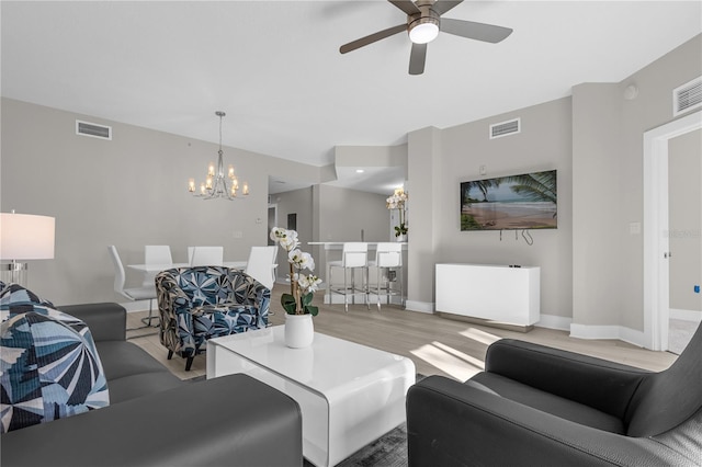 living room with ceiling fan with notable chandelier and light hardwood / wood-style flooring