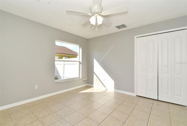 unfurnished bedroom featuring light tile patterned floors, a textured ceiling, a closet, and ceiling fan