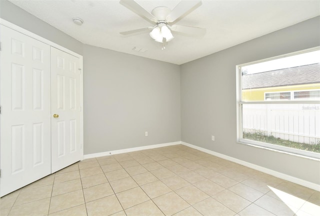 unfurnished bedroom with ceiling fan, light tile patterned flooring, a closet, and multiple windows