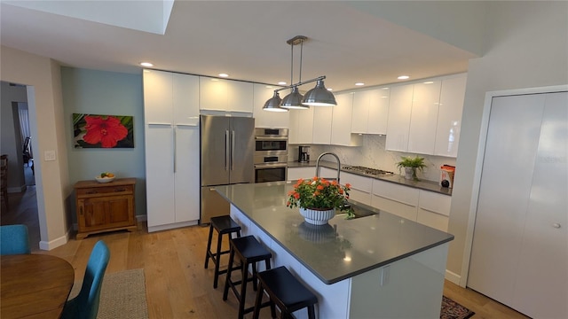 kitchen featuring pendant lighting, white cabinets, light hardwood / wood-style floors, a kitchen island, and stainless steel appliances