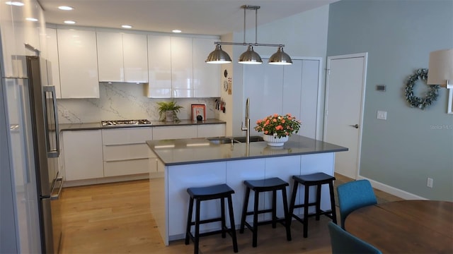 kitchen featuring white cabinets, appliances with stainless steel finishes, hanging light fixtures, and an island with sink