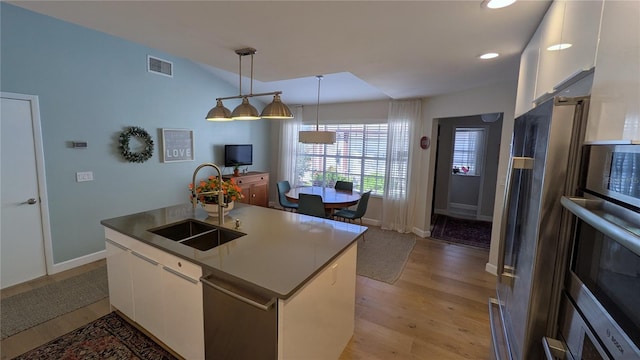 kitchen with sink, decorative light fixtures, a center island with sink, white cabinets, and light hardwood / wood-style floors